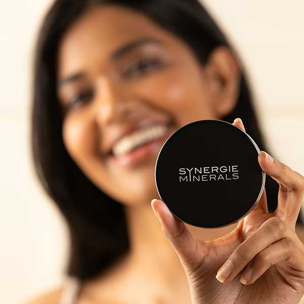 Woman holding Synergie Minerals makeup to the camera