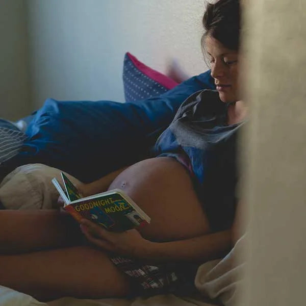 Pregnant woman lying in bed reading a book